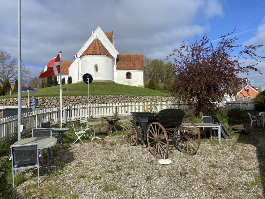 Kirke og forhave med flag på vandrehjem i Lindelse på Langeland